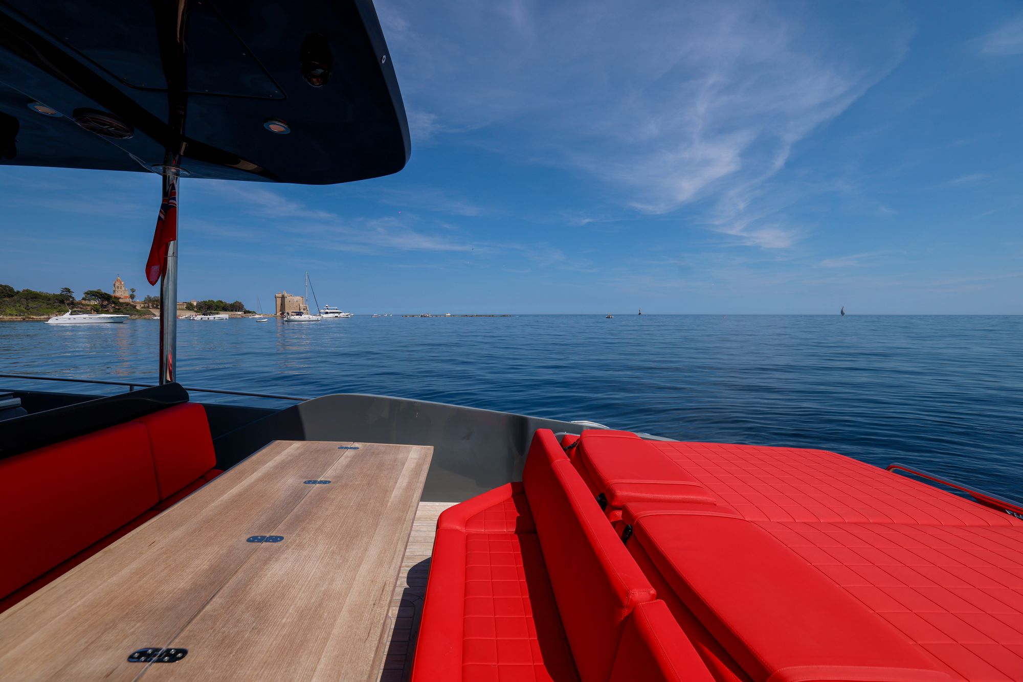 The aft deck at anchor, teak table and red seating, the Lérins fort across flat water