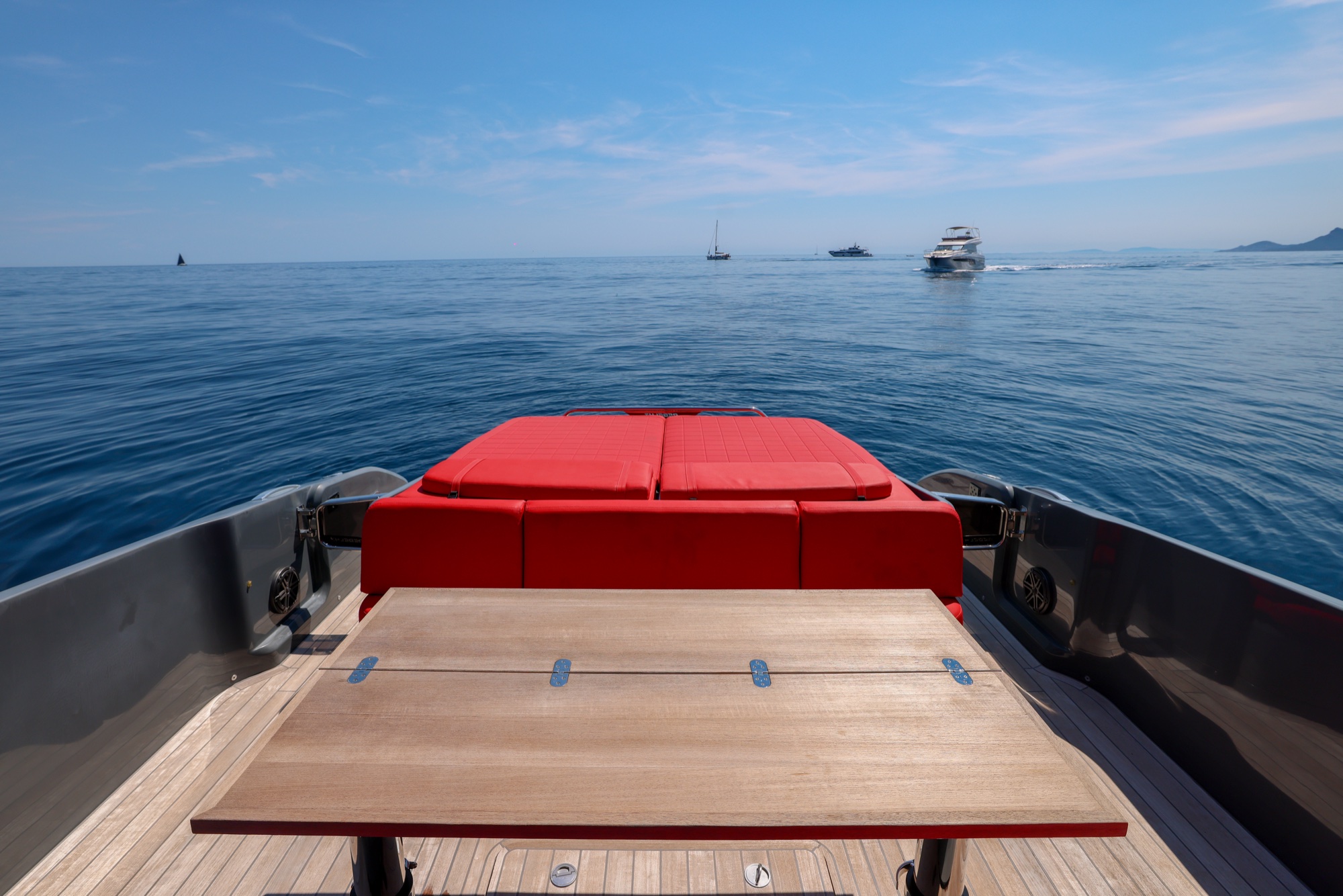 The teak table and red sunbeds of Queen of Hearts looking astern over calm water