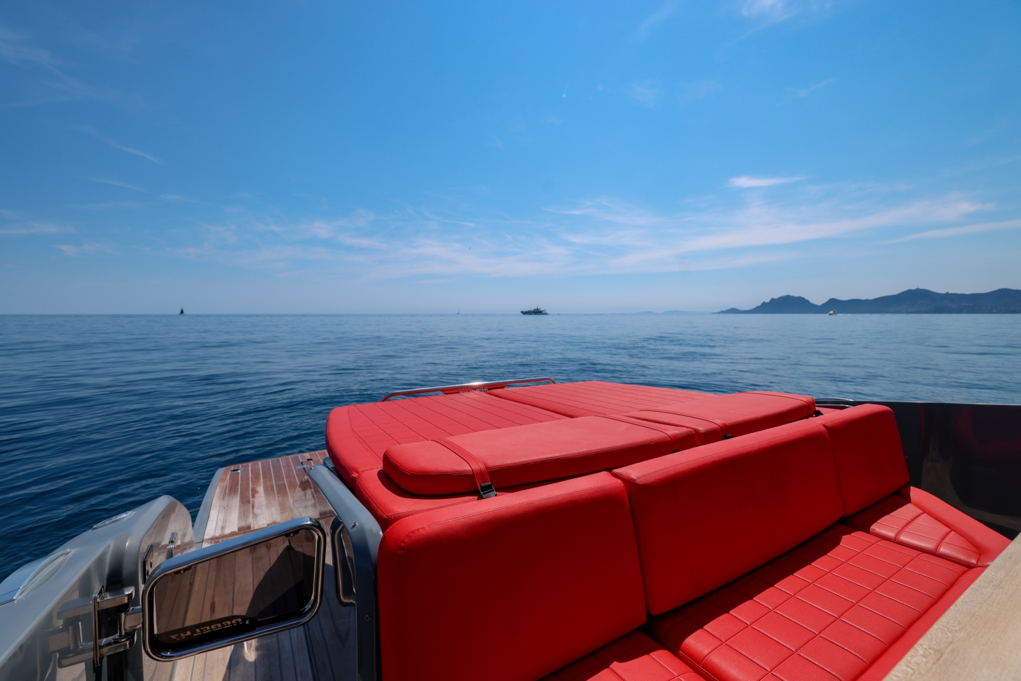 The red aft sofa of Queen of Hearts, the coast's high silhouette in the distance