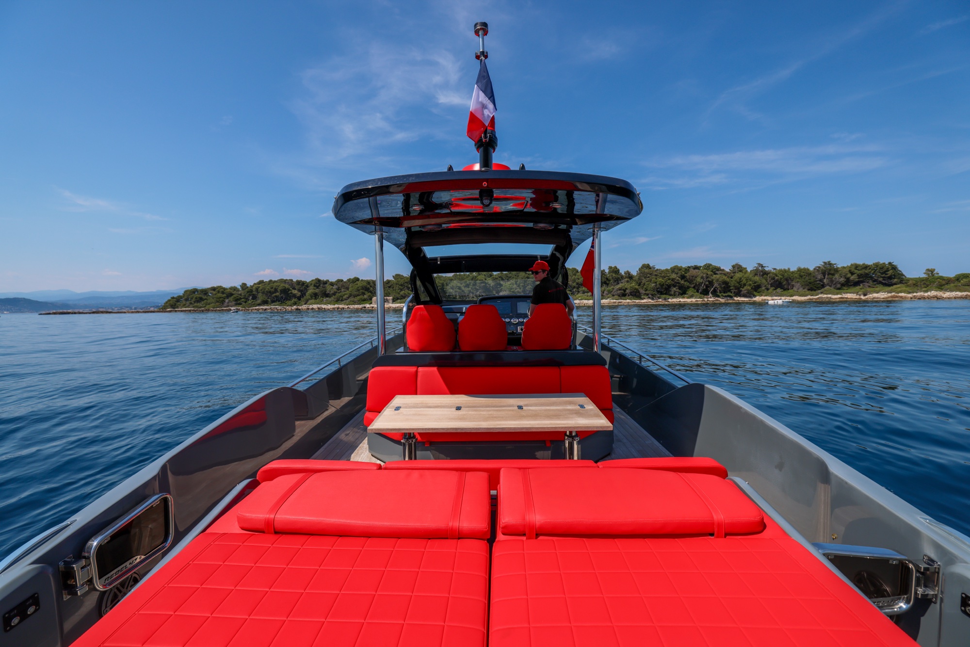 The deck of Queen of Hearts under her flag, the wooded shore of the bay beyond