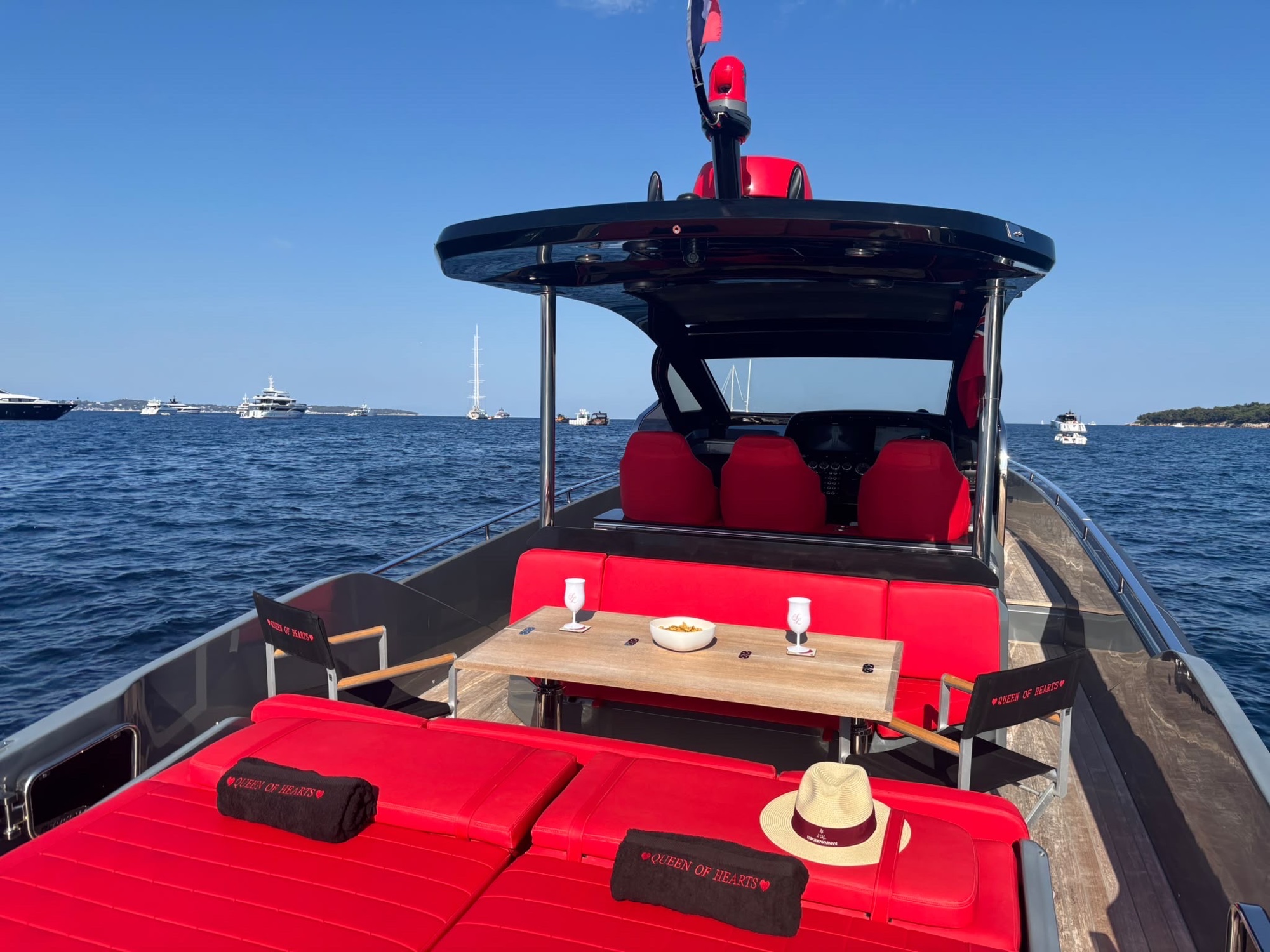 Looking forward along the deck of Queen of Hearts — red sunbeds, teak table and helm under the T-top