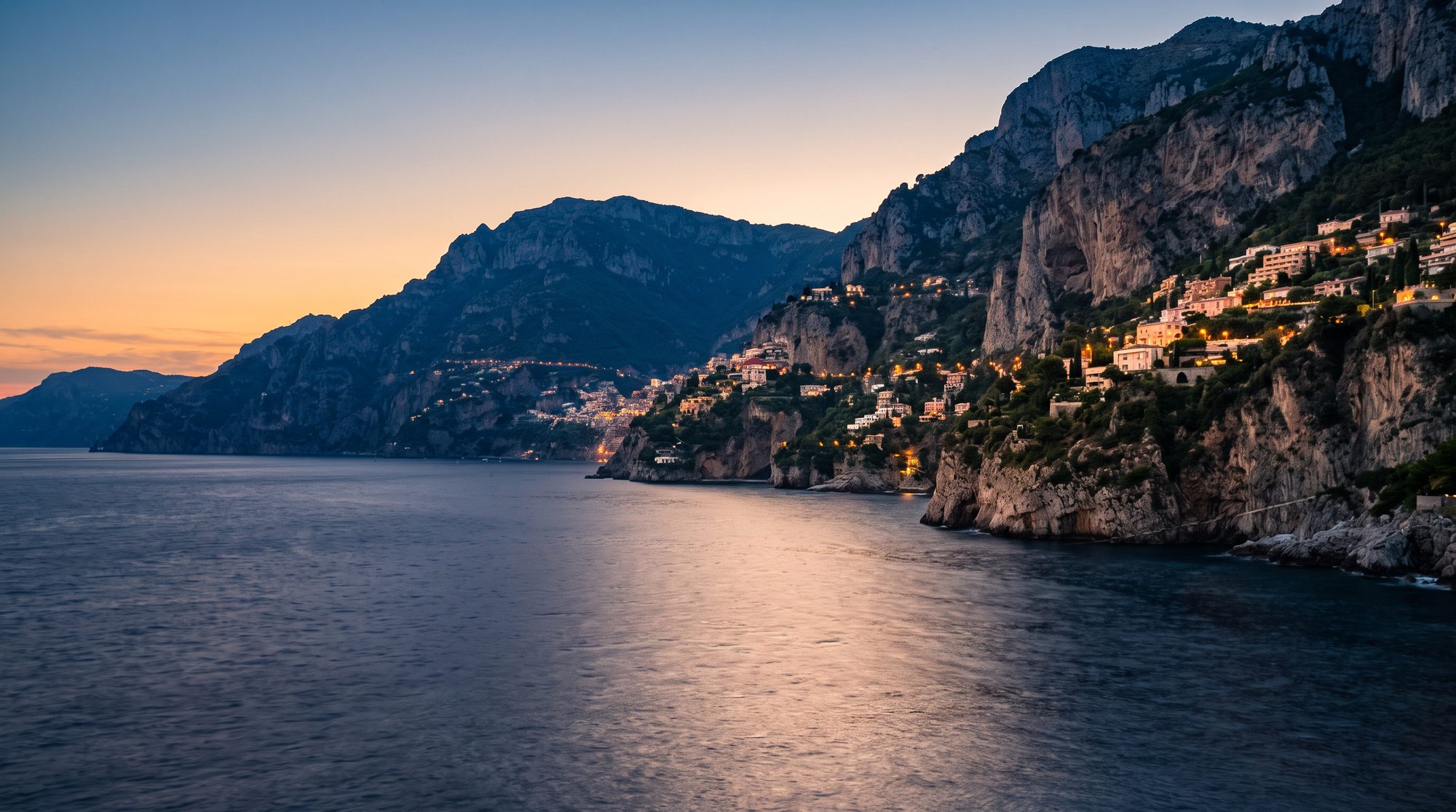 The mountainous coast beside Monaco at dusk, lights beginning to show on the terraces