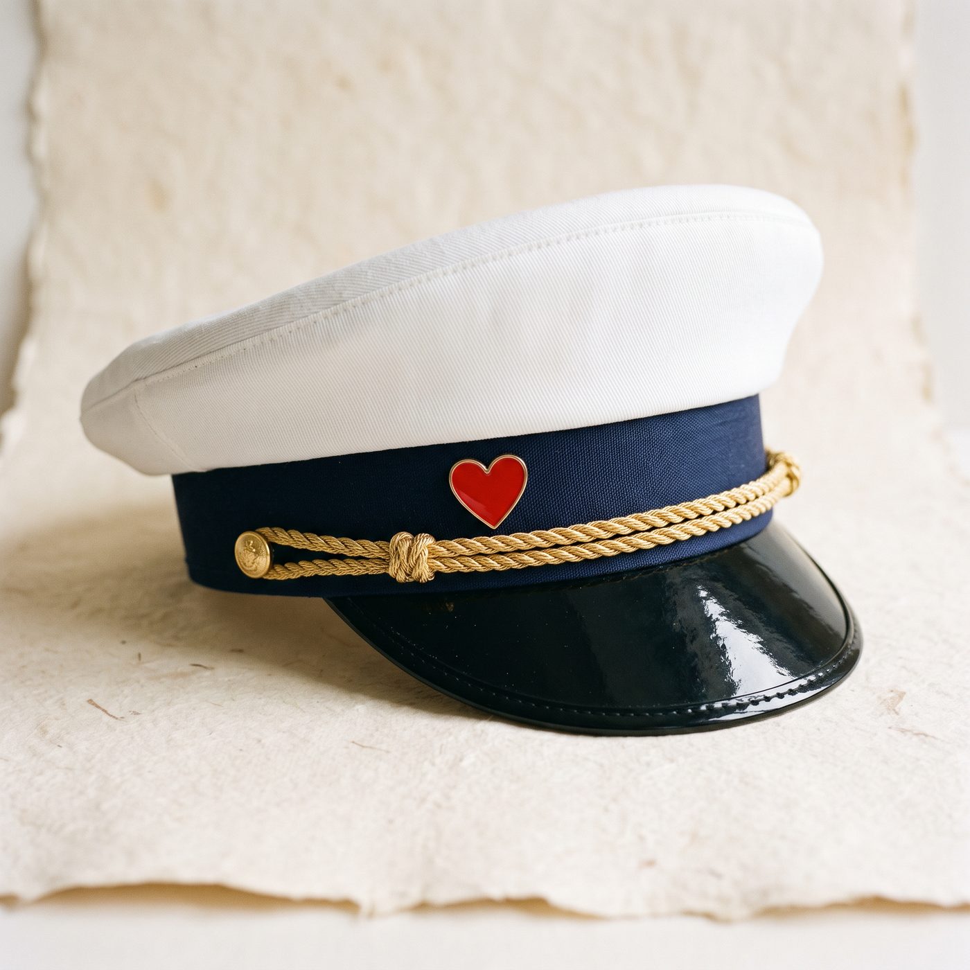White captain’s hat with navy band, gold braid and a small red enamel heart