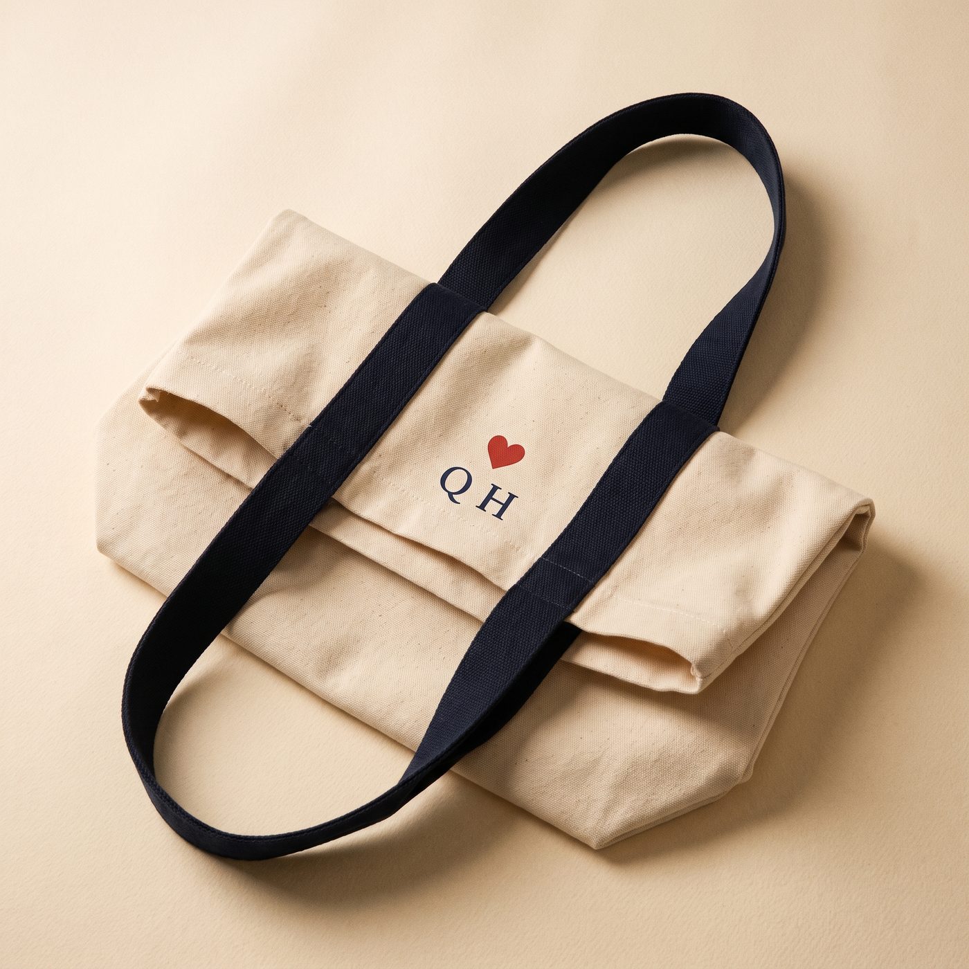Ecru canvas tote bag with navy handles and a small Q♥ mark